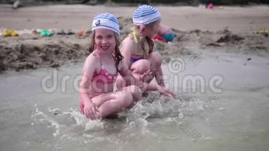两个女孩在海滩上泼水。 在炎热的夏日里，双胞胎倒着水，孩子们的笑声和好心情